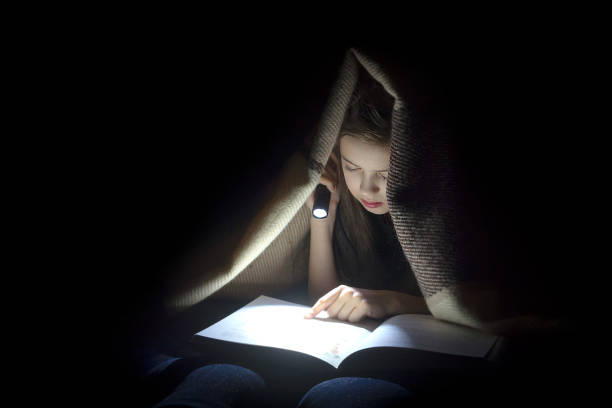 girl with a flashlight reading a book.